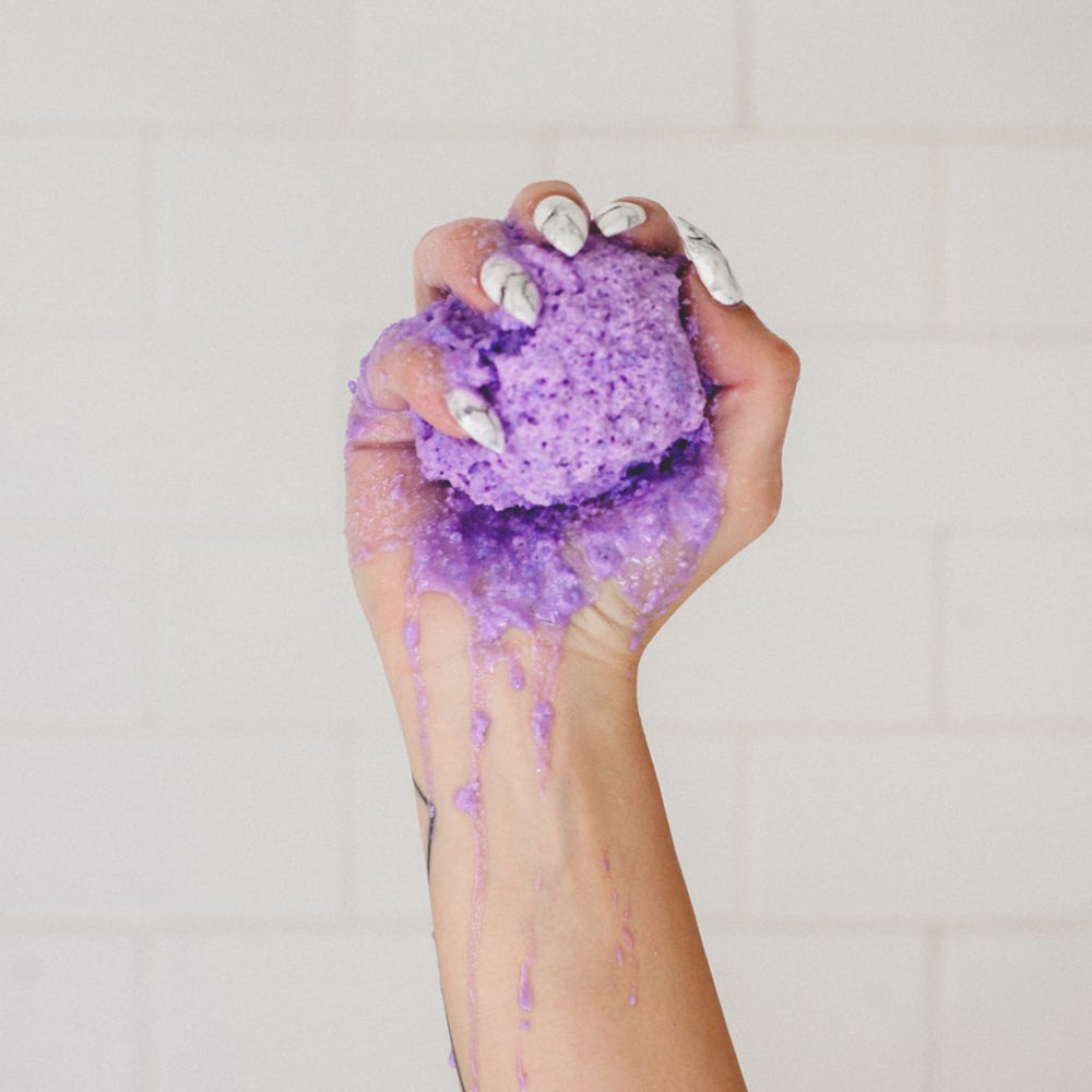Hand holding a purple Kush Queen CBD Bath Bomb that is dissolving and running down their arm.