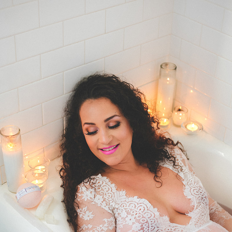 A mom in a white bath tub with candles enjoying a Kush Queen CBD Bath Bomb
